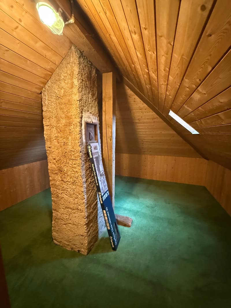 A room with a fireplace, wooden ceiling, green carpet, and a large stone pillar