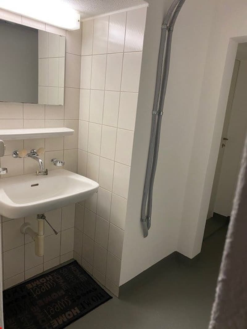Bathroom with white tiles, white sink, mirror, and black mat