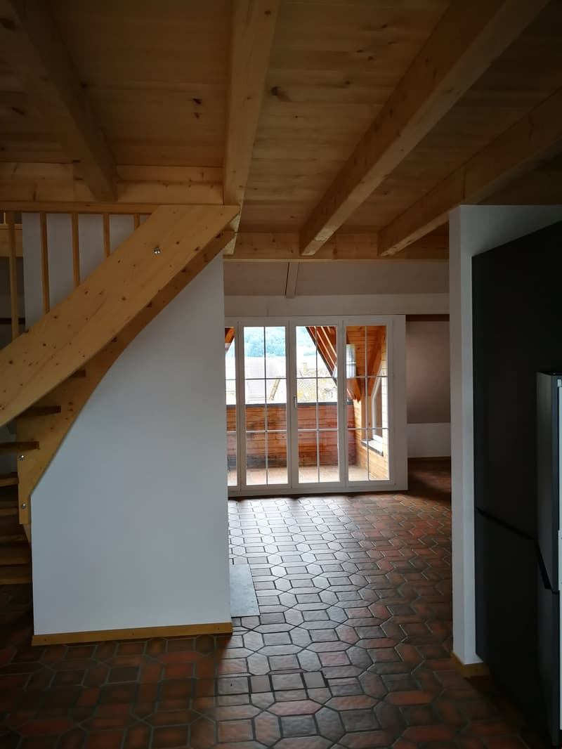 Empty room with wooden ceiling, white walls, wooden staircase, and hexagonal tile flooring. There is a glass door leading to an outdoor area.