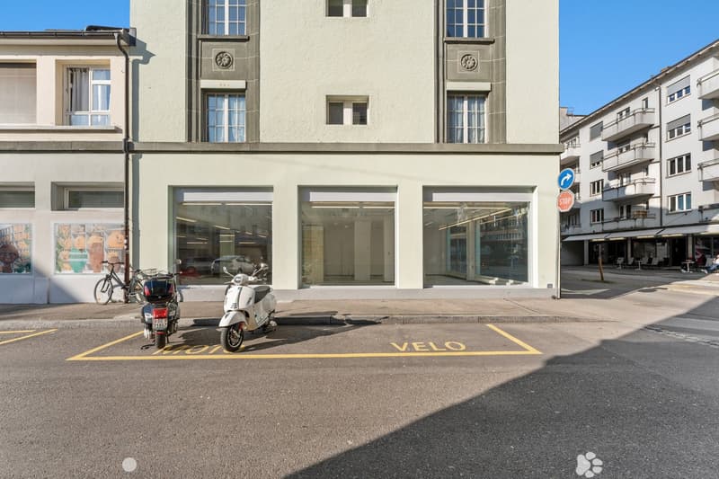 2 story building, white exterior, glass windows, 3 glass doors, bicycles parked in front, stop sign, parking space