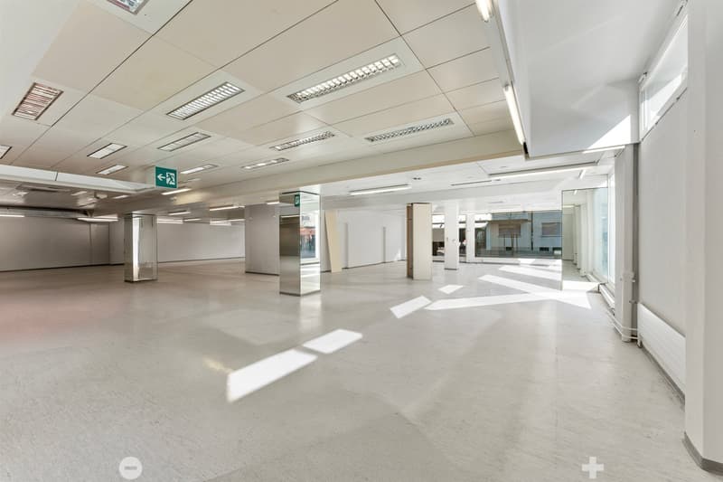 Empty room with white walls, white floor, glass windows, metal columns, ceiling lights, emergency exit sign