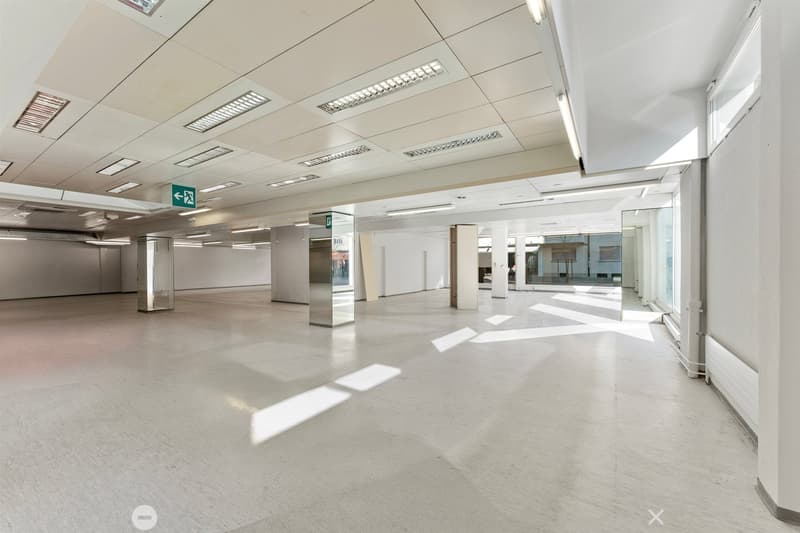 Empty room with white walls, white floor, glass windows, metal columns, ceiling lights, emergency exit sign