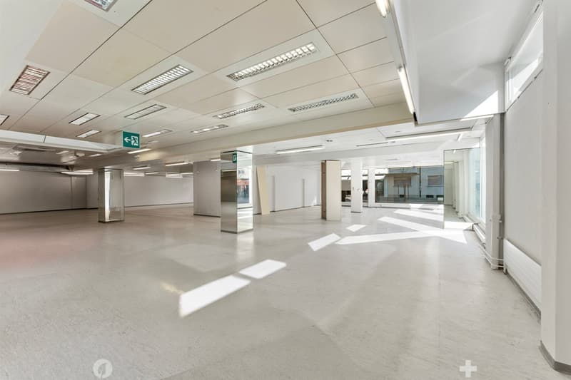 Empty room with white walls, white floor, glass windows, metal columns, ceiling lights, emergency exit sign