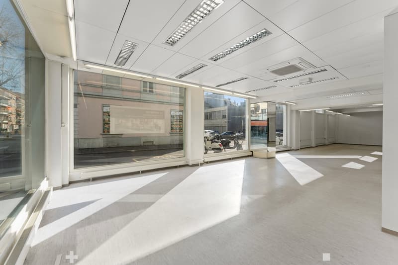 Empty room with large windows, white walls, white ceiling, white floor, and visible ceiling lights