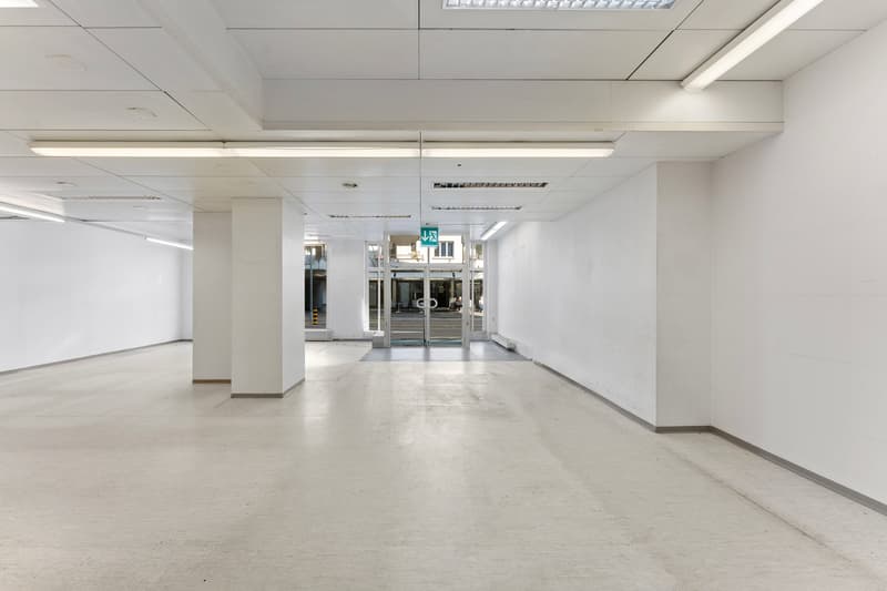 Empty room with white walls, white ceiling, white floor, and white pillars. There is a glass door at the end of the room.