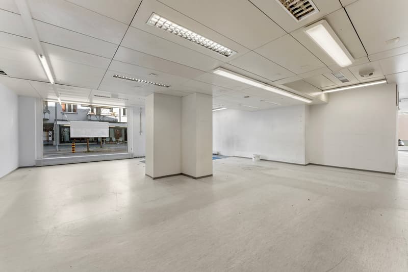 Empty room with white walls, ceiling, and floor, large windows, and fluorescent lights.