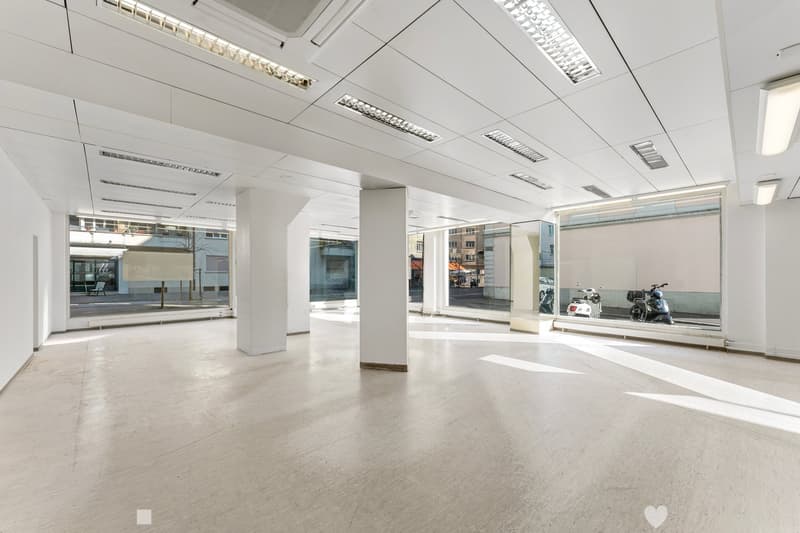 Empty room with white walls, ceiling, and floor, large windows, two white pillars, ceiling lights