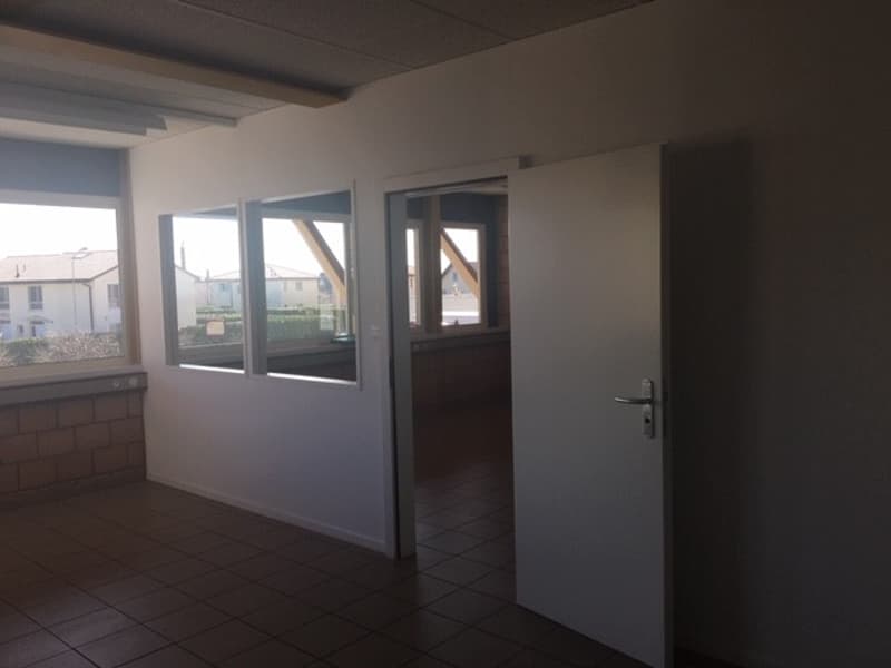 A room with white walls, tiled floor, large windows and an open door leading to another room