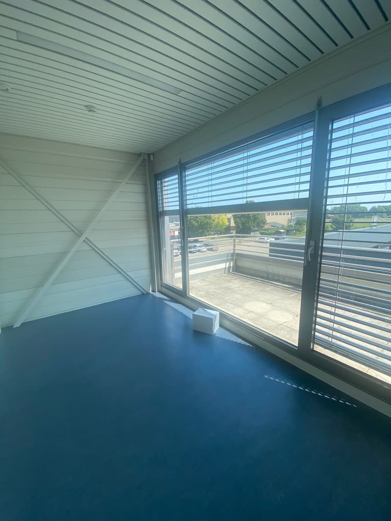 empty room with white walls, wooden beam, white ceiling, balcony, large window, outside view, balcony railing, and blue floor