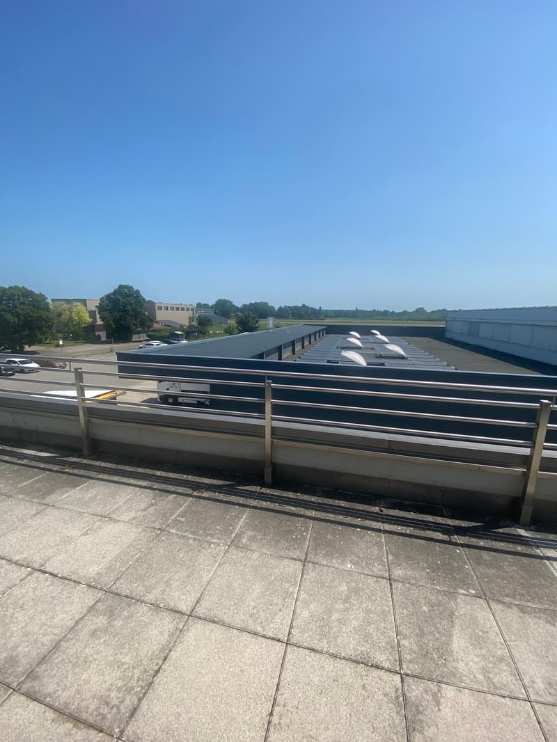 Roof terrace, fenced with stainless steel railing, concrete floor, buildings in the distance, clear sky