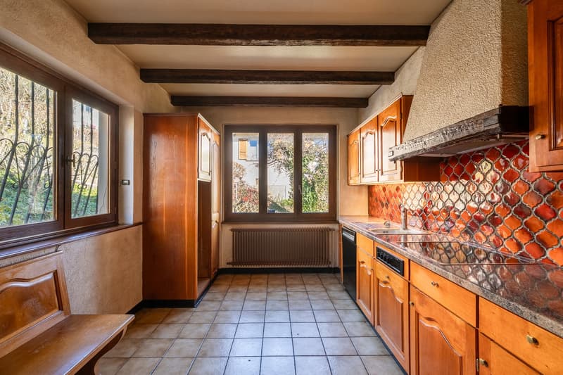 Wooden cabinetry, tiled floor, window with grills, kitchen counter, tiled backsplash, sink, faucet, dishwasher, electric hob