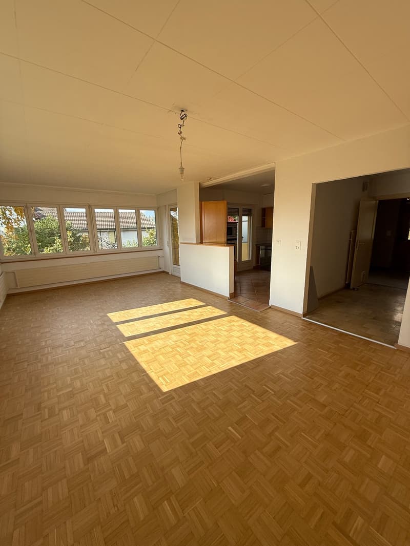 empty room, hardwood floors, large windows, wooden cupboard, white walls, kitchen access, heater under windows