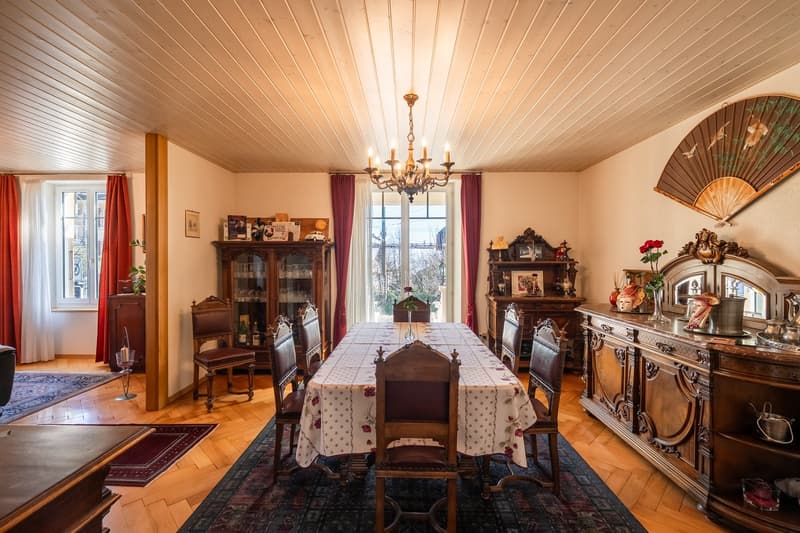 dining room, chandelier, dining table with chairs, glass windows with curtains, wooden cabinets, shelves, floral design tablecloth, rug
