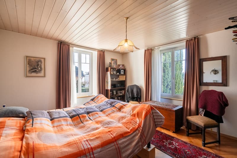 Bedroom with bed, wooden floor, wall paintings, curtains, chandelier, wooden chair, wooden desk, rug, cabinet