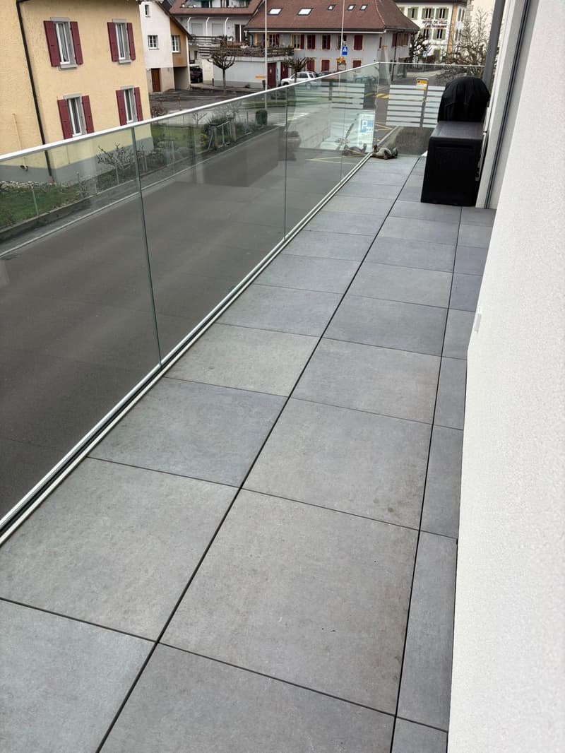 Outdoor terrace with glass railings and tiled flooring, adjacent to a building