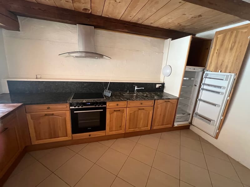 Wooden cabinets, black granite countertop, gas stove, range hood, refrigerator, tiled floor