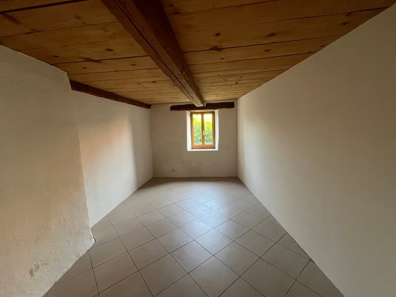 This image shows a room with a wooden ceiling and white walls. The room has a tiled floor and a window that provides natural light. The room appears to be empty and ready for furnishing or use.