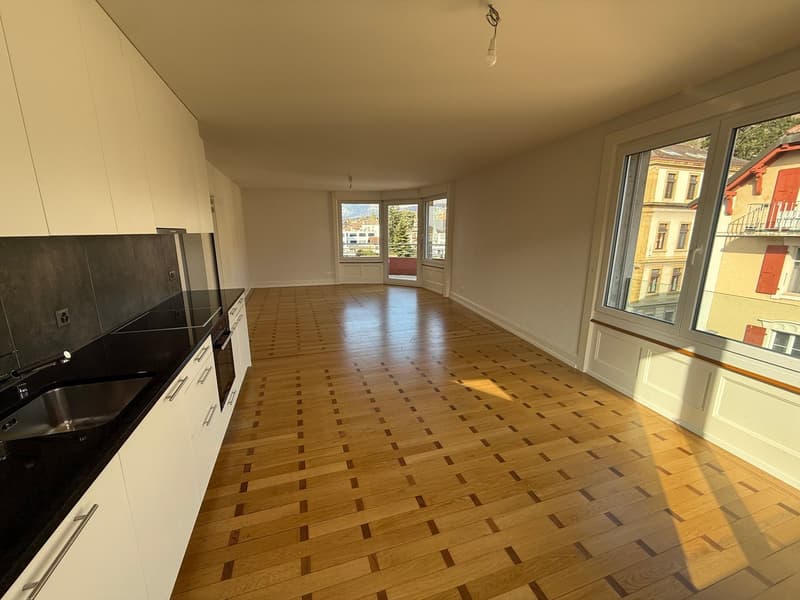empty room, wooden floor, white walls, large windows, kitchen area with sink and cabinets