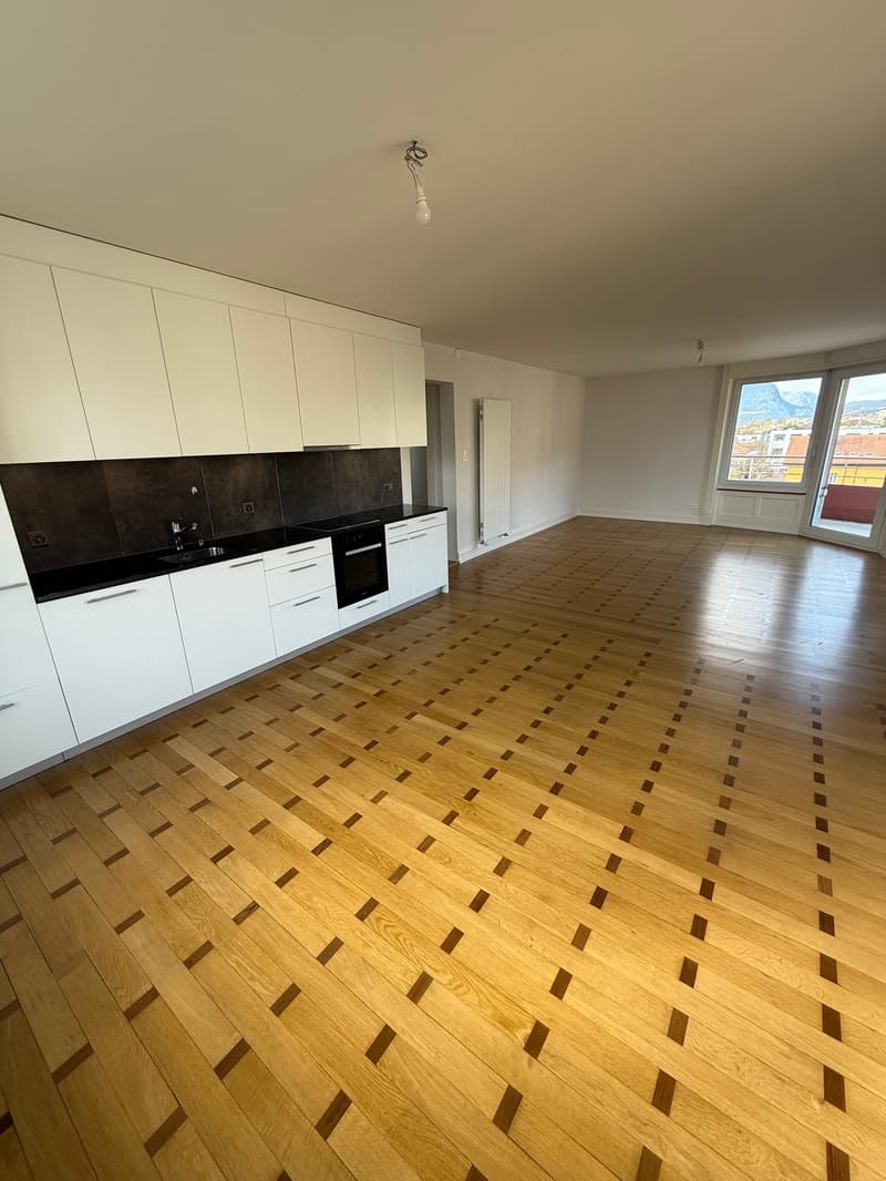 Empty room with wooden floor, white cabinets, black countertops, white radiator, glass doors, balcony, mountain view
