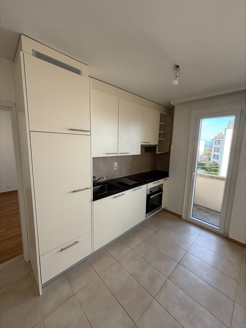 modern kitchen with white cabinets, black countertops, stainless steel sink, oven, and a sliding glass door leading to a balcony