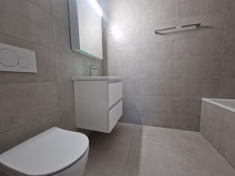modern bathroom with white tiles, white sink, silver faucet, white toilet, bathtub, mirror