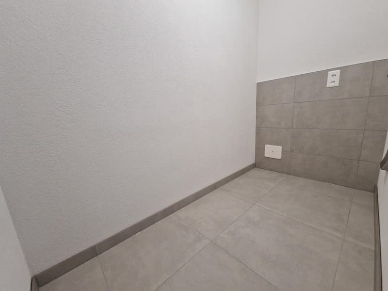 Empty room with white walls and gray tiles, power outlet on the wall