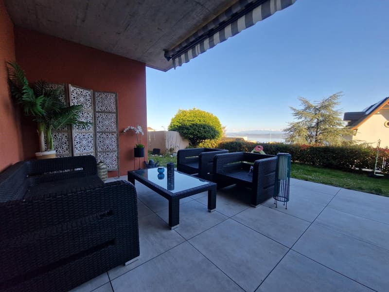 Terrace with wicker furniture, glass table, plants, and a view of the mountains