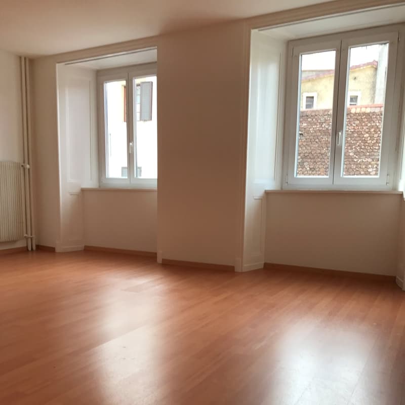 Empty room, wooden floor, white walls, two windows, white shutters, radiator