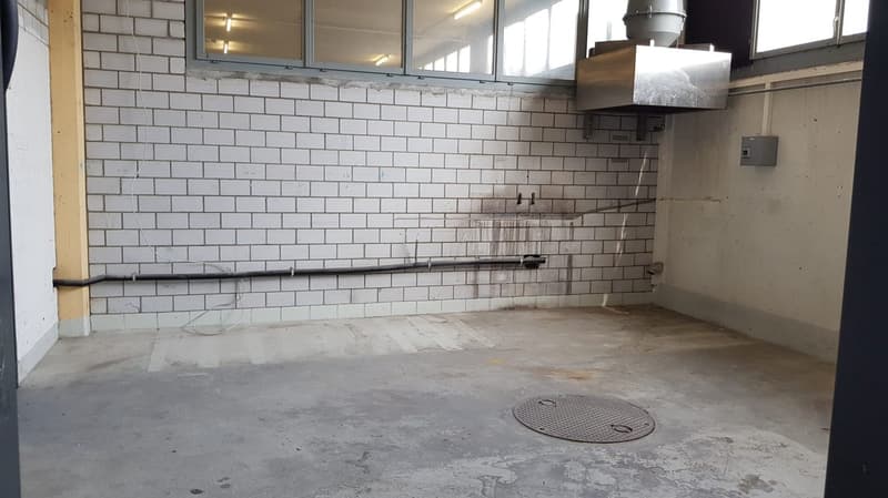 Empty room with white brick walls, concrete floor, exhaust vent, wires and pipes attached to the wall, manhole cover on the floor.