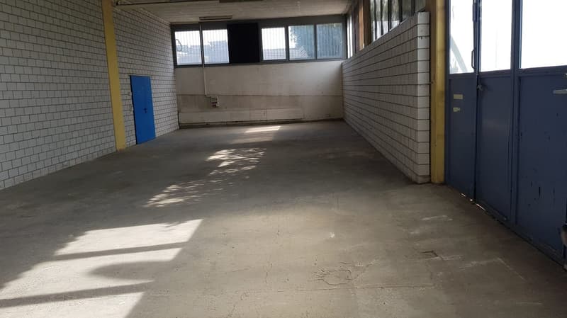 Empty room with white tiled walls, concrete floor, large window on back wall, doors on the sides.