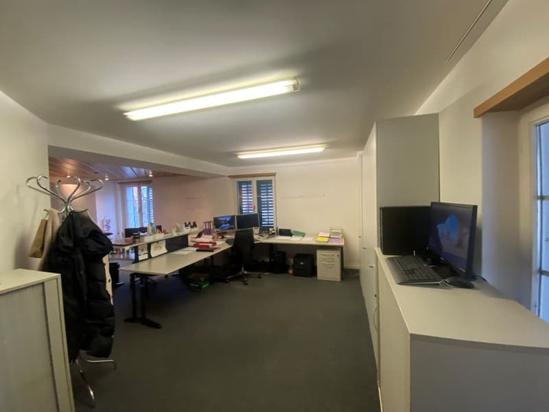 Empty office room with desks, chairs, monitors, keyboards, storage cabinets and ceiling lights