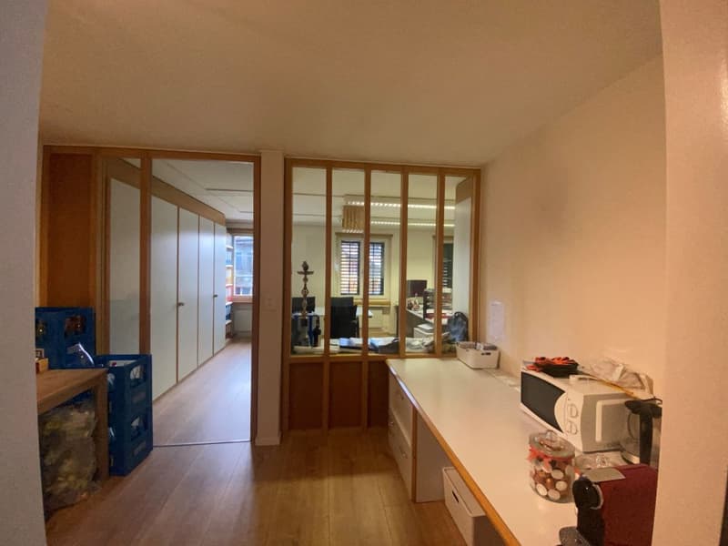 corridor leading to a room with white countertops and a microwave, glass doors, wooden floors, cabinets