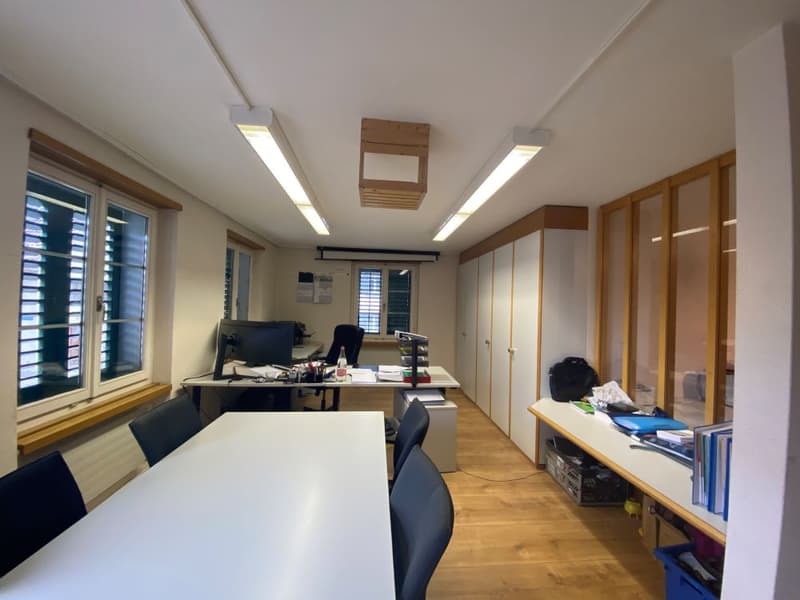 Large room with wooden floors, two long desks, chairs, monitors, cabinets, and white walls