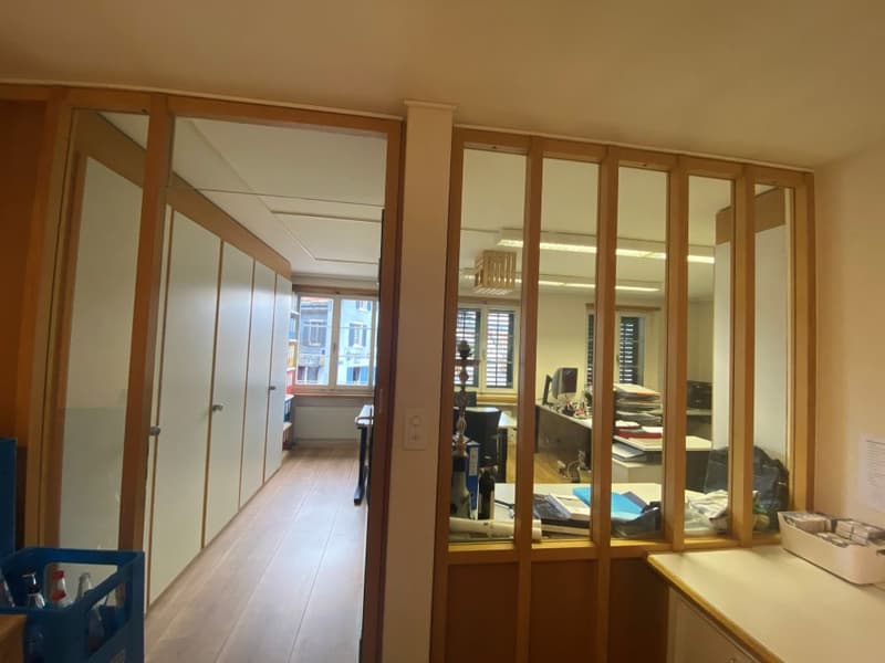 Empty office room, wooden door, glass partition wall, wooden desk, glass windows, office equipment, wooden floor.
