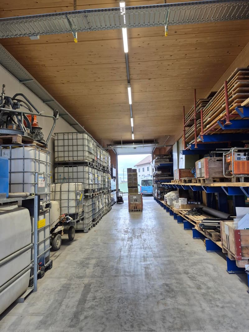 Warehouse with concrete floor, wooden ceiling, metal shelving, storage boxes, and machinery