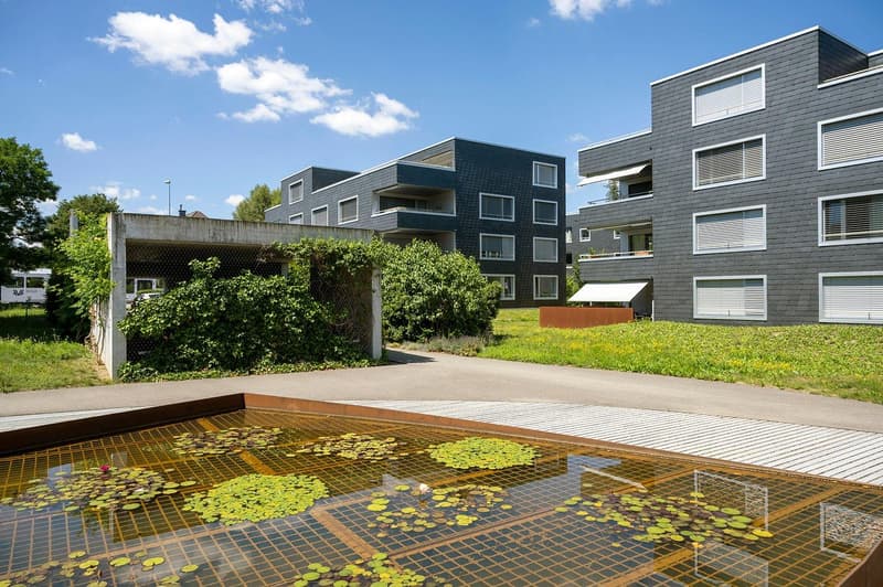 Modern residential complex with gray exterior, large pond in the foreground