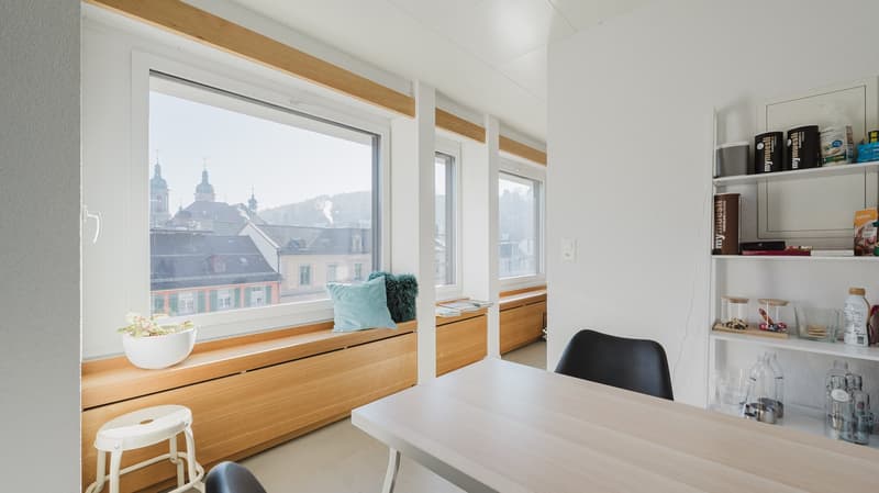 modern interior, large windows, wooden bench, white table, black chairs, white stool, white walls, wooden floor