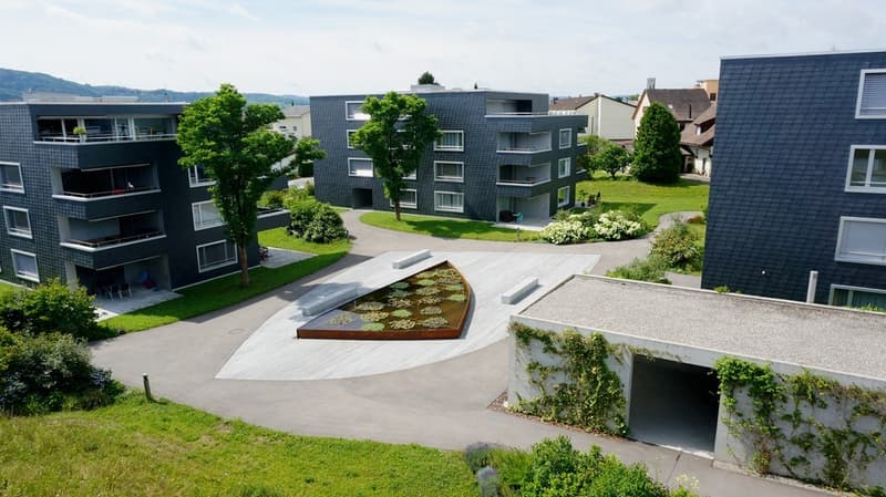 Aerial view of a residential building complex with a garden and a pond in the middle