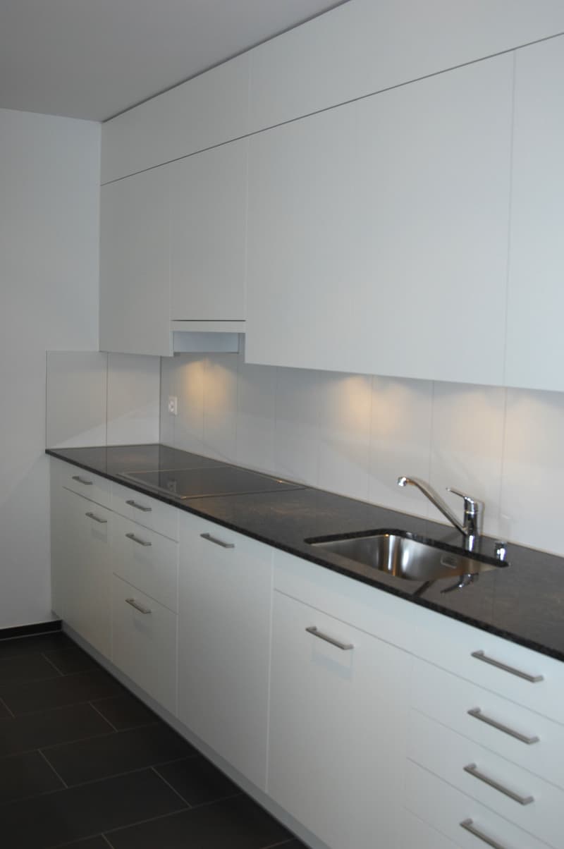 modern kitchen with white cabinets, black countertops, stainless steel sink, and a gas stove
