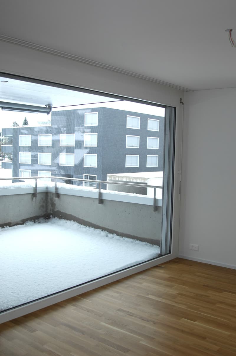 large glass door, balcony, wooden floor, white walls, view of building