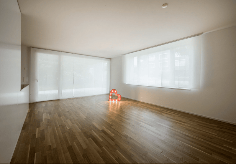 Empty room with wooden floor, white walls, large windows, and a heart-shaped light fixture.