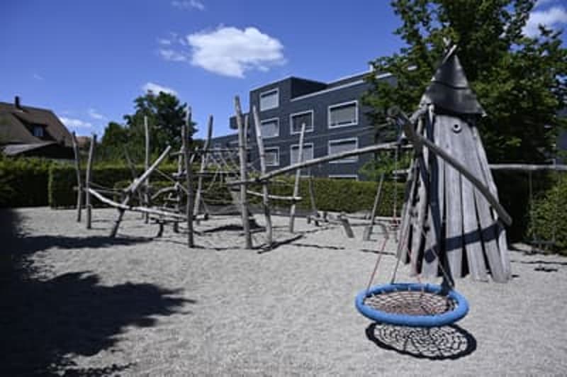 Outdoor playground with wooden structures, swings, and a sand pit.