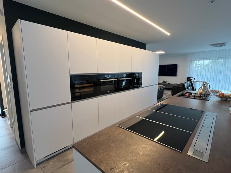 Modern kitchen with white cabinetry, induction stove, double oven, kitchen island, open floor plan