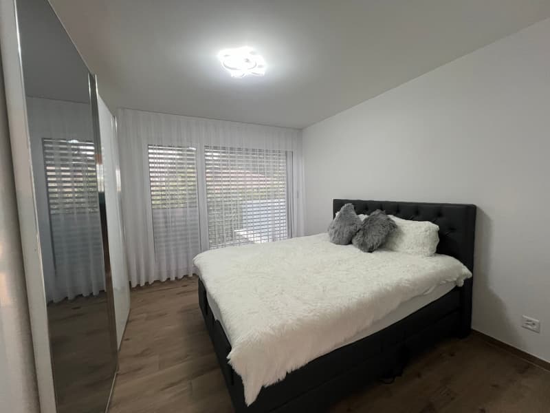modern bedroom with white walls, wooden floor, large bed, and windows with white curtains