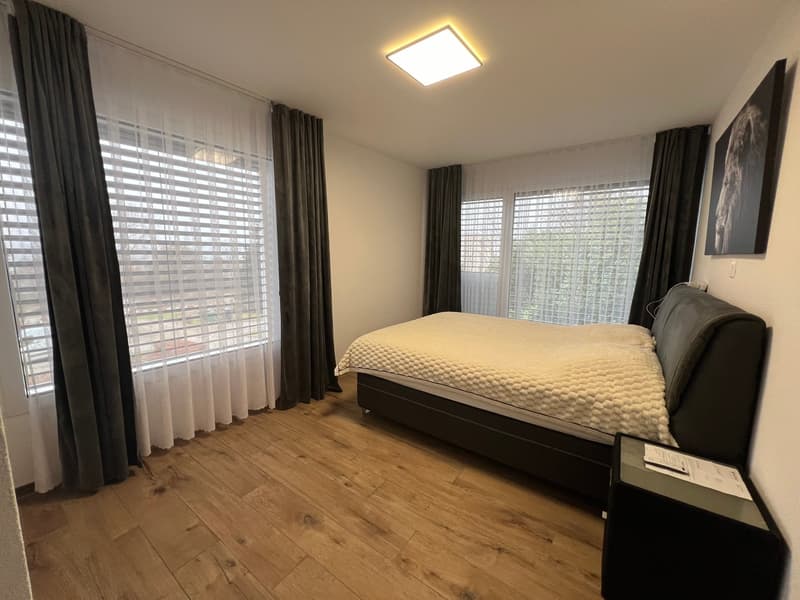 Bed, two windows with curtain, wooden floor, square wall lamp, nightstand