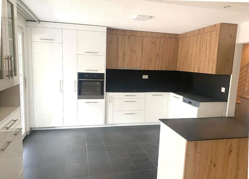Modern kitchen with white cabinets, black countertops, tiled floor, integrated dishwasher, washing machine, and an oven.