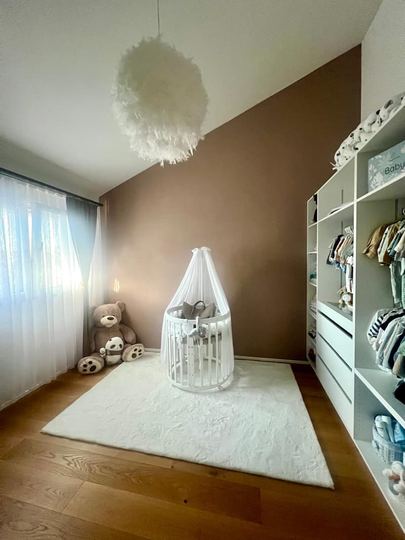 baby room with crib, light fixture, plush bear, white rug, shelves with clothes
