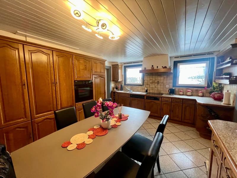 Kitchen with wooden cabinets, a tiled floor, granite countertops, a dining table with chairs, an oven, a sink with faucet, and a faucet mounted on the wall. Two windows with natural light.