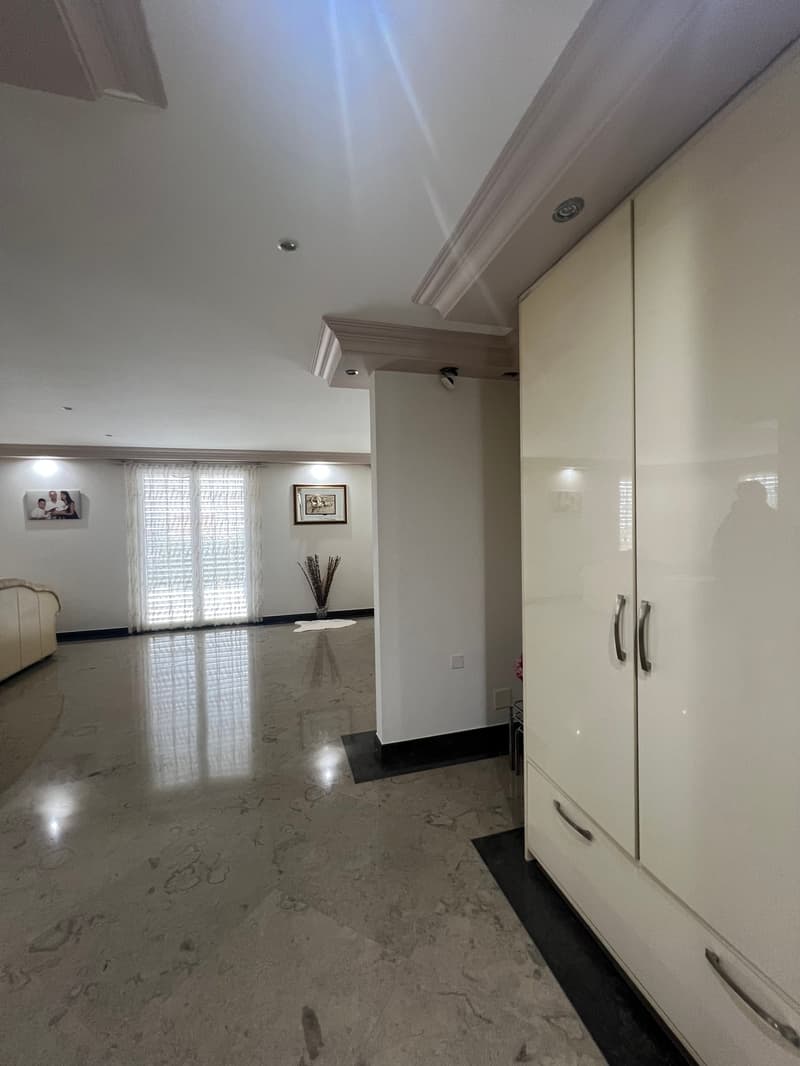 Empty room with white walls, large windows, marble floor, large white wardrobe, picture frames on the wall, and a plant in a vase.