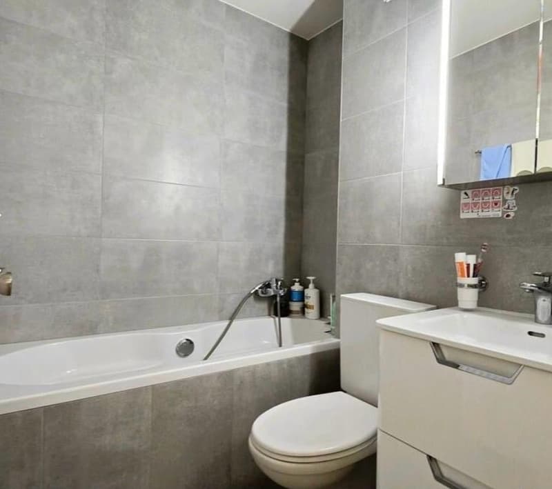 Bathroom with bathtub, toilet, sink, mirror, and gray tiles
